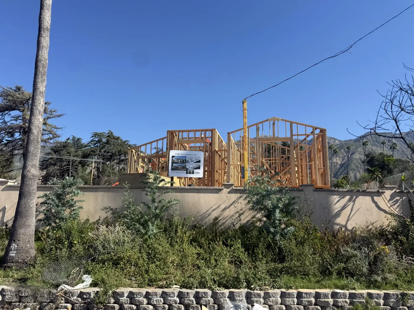 PMK Development jobsite sign in front of the framed home on Las Flores Drive, with the San Gabriel foothills behind.